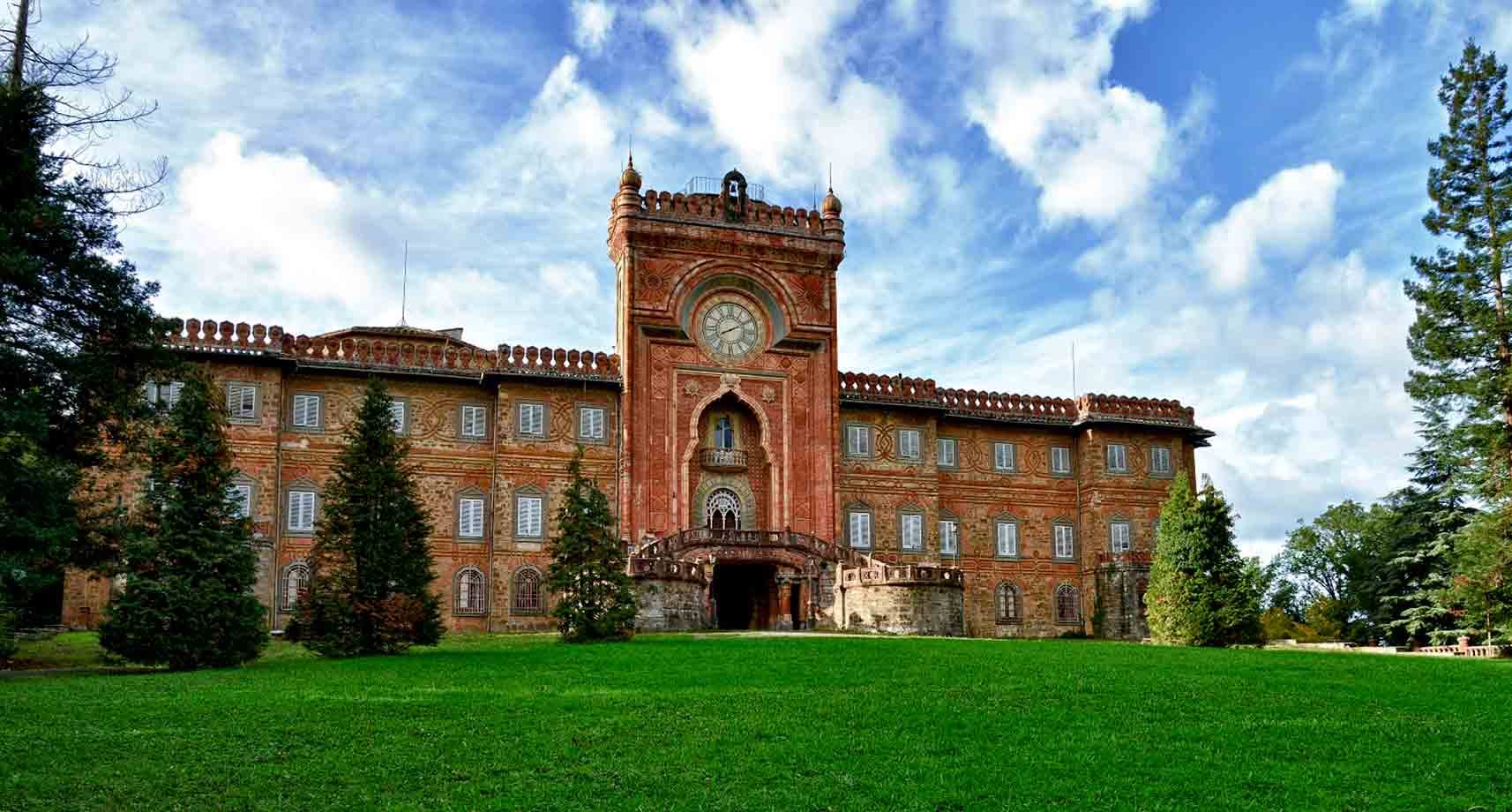 Castello di Sammezzano, facciata in mattoni rossi con orologio, prato verde e pini