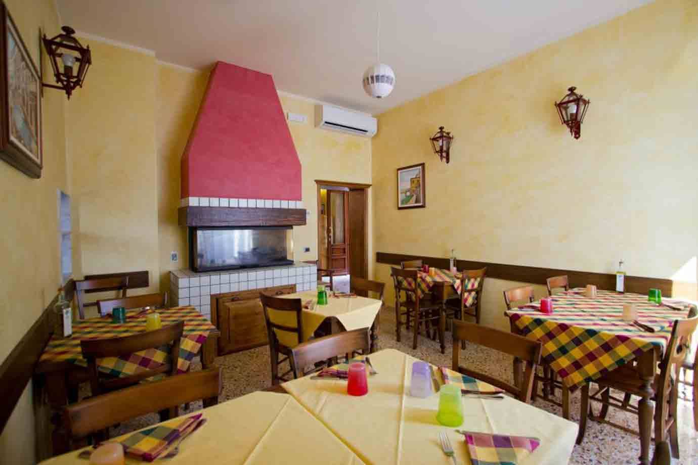 Sala da pranzo con tavoli apparecchiati, tovaglie gialle e camino dipinto di rosa