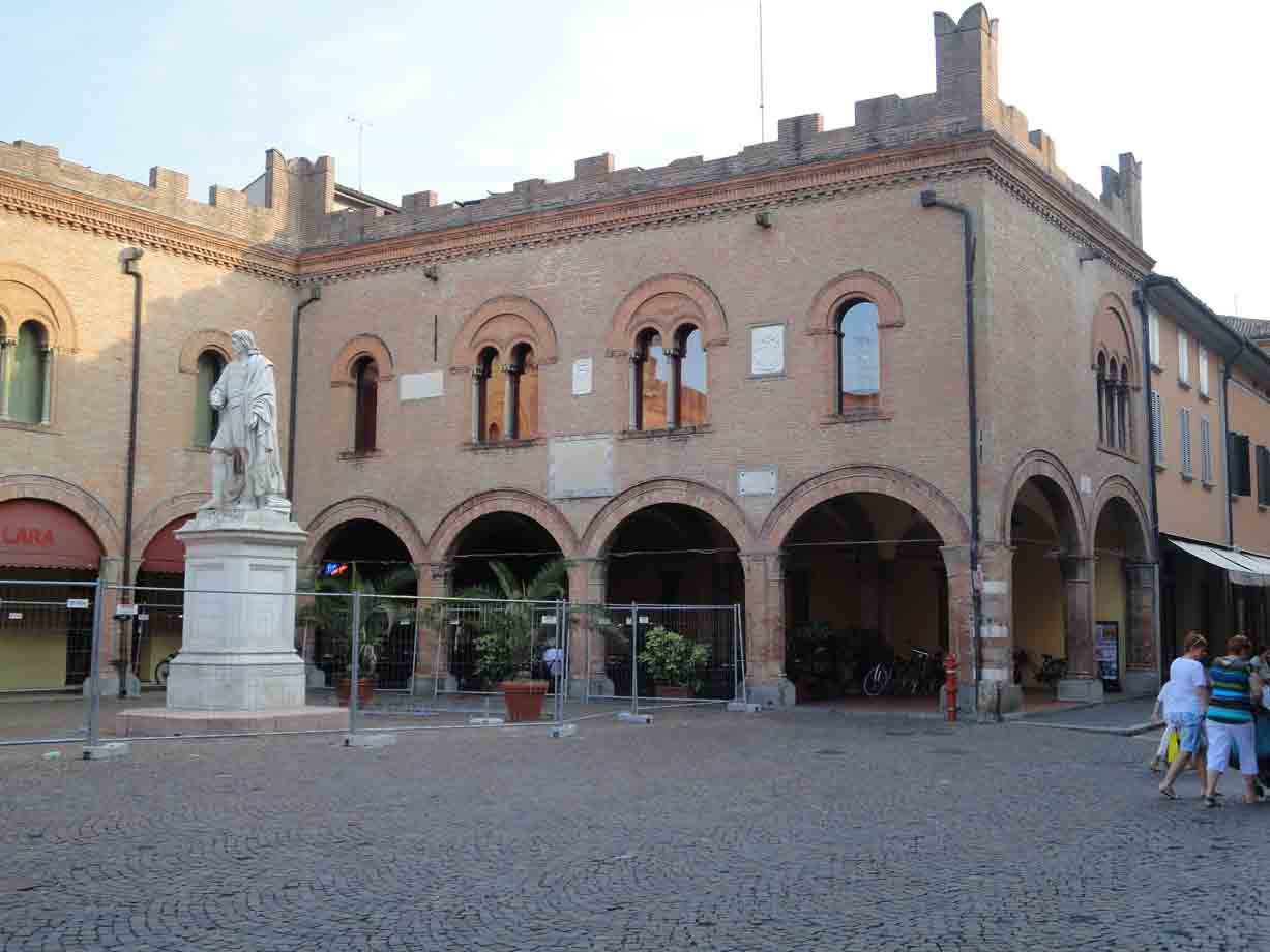 Statua in marmo davanti a un palazzo medievale in mattoni con portici e merlature