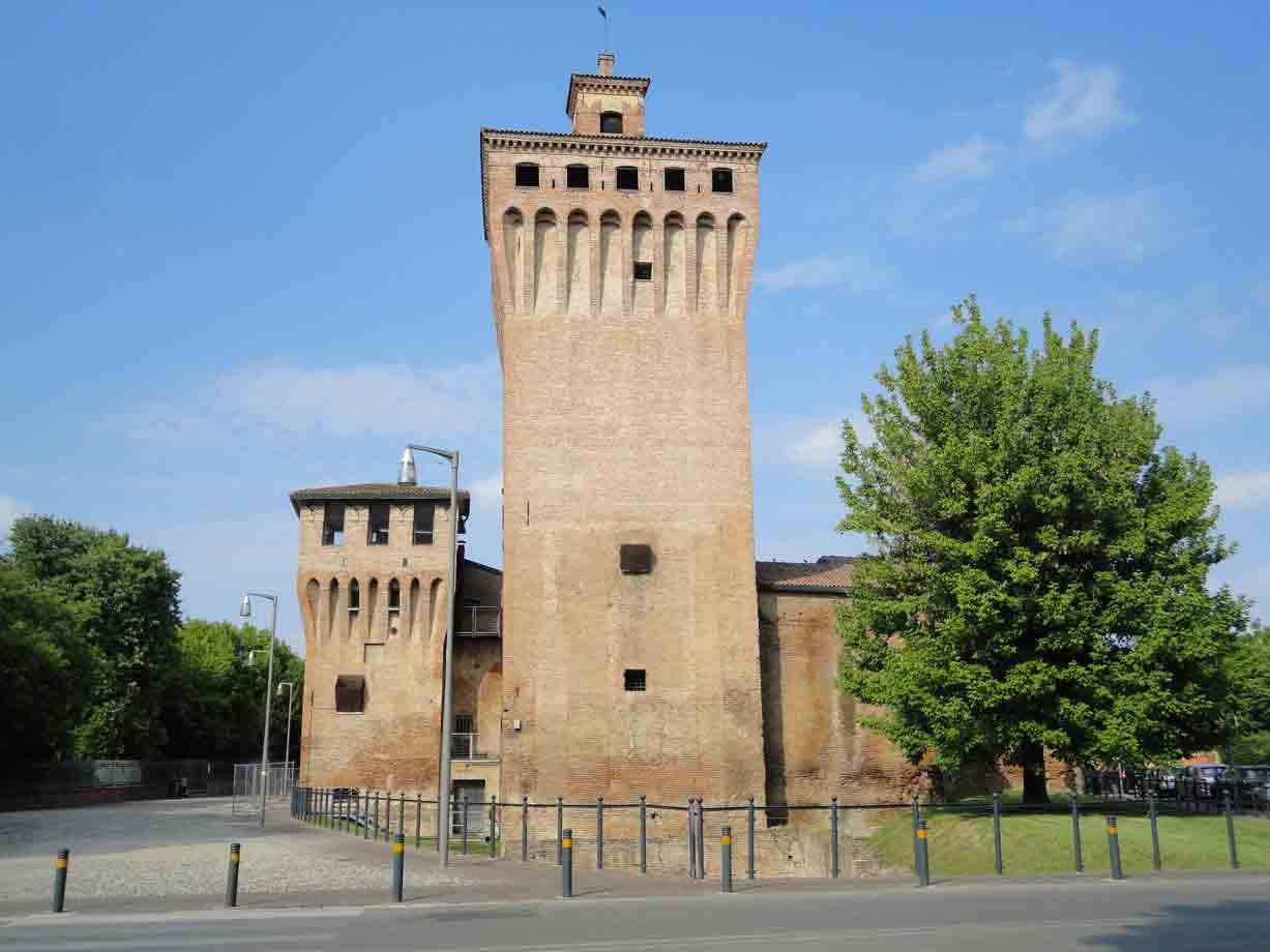 Torre in mattoni della Rocca di Cento sotto cielo azzurro, alberi verdi ai lati