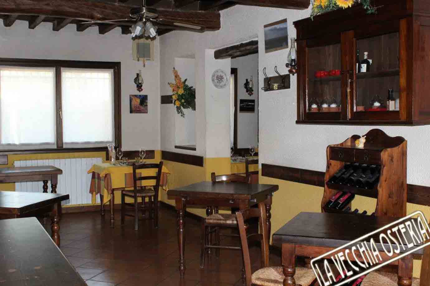 Sala rustica della trattoria La Vecchia Osteria con tavoli in legno e bottiglie