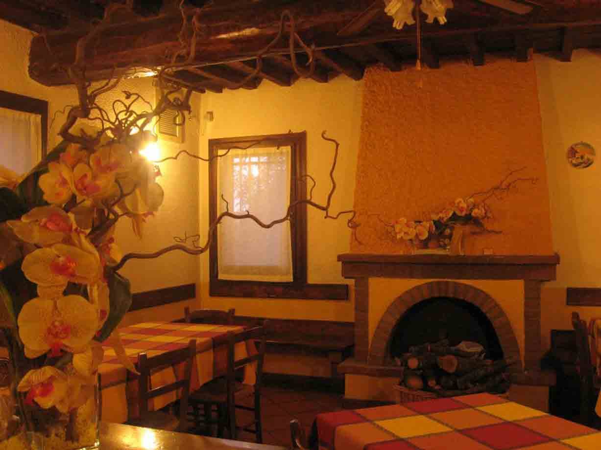 Sala di trattoria con caminetto in mattoni, travi in legno e orchidee gialle