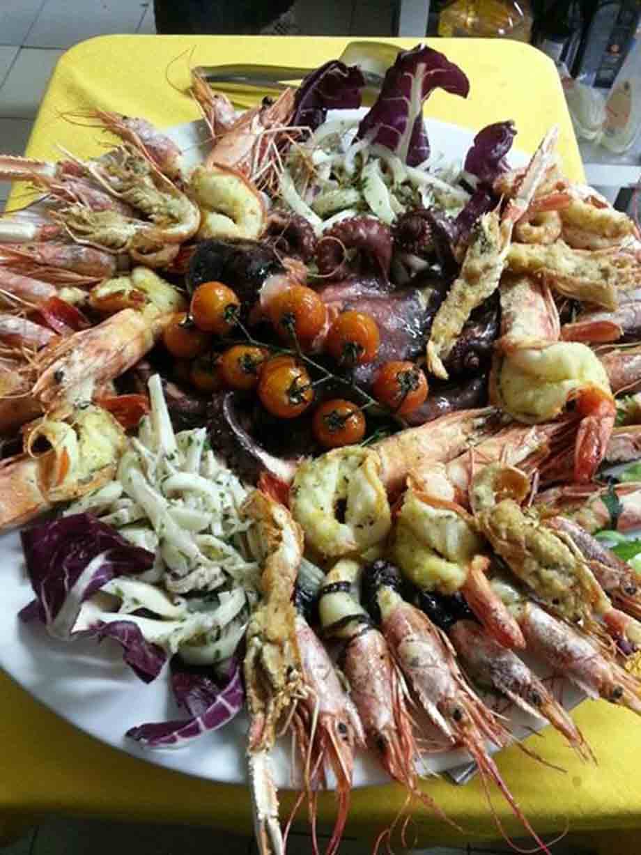 Piatto di frutti di mare con gamberoni, polpo, calamari e pomodorini su tovaglia gialla