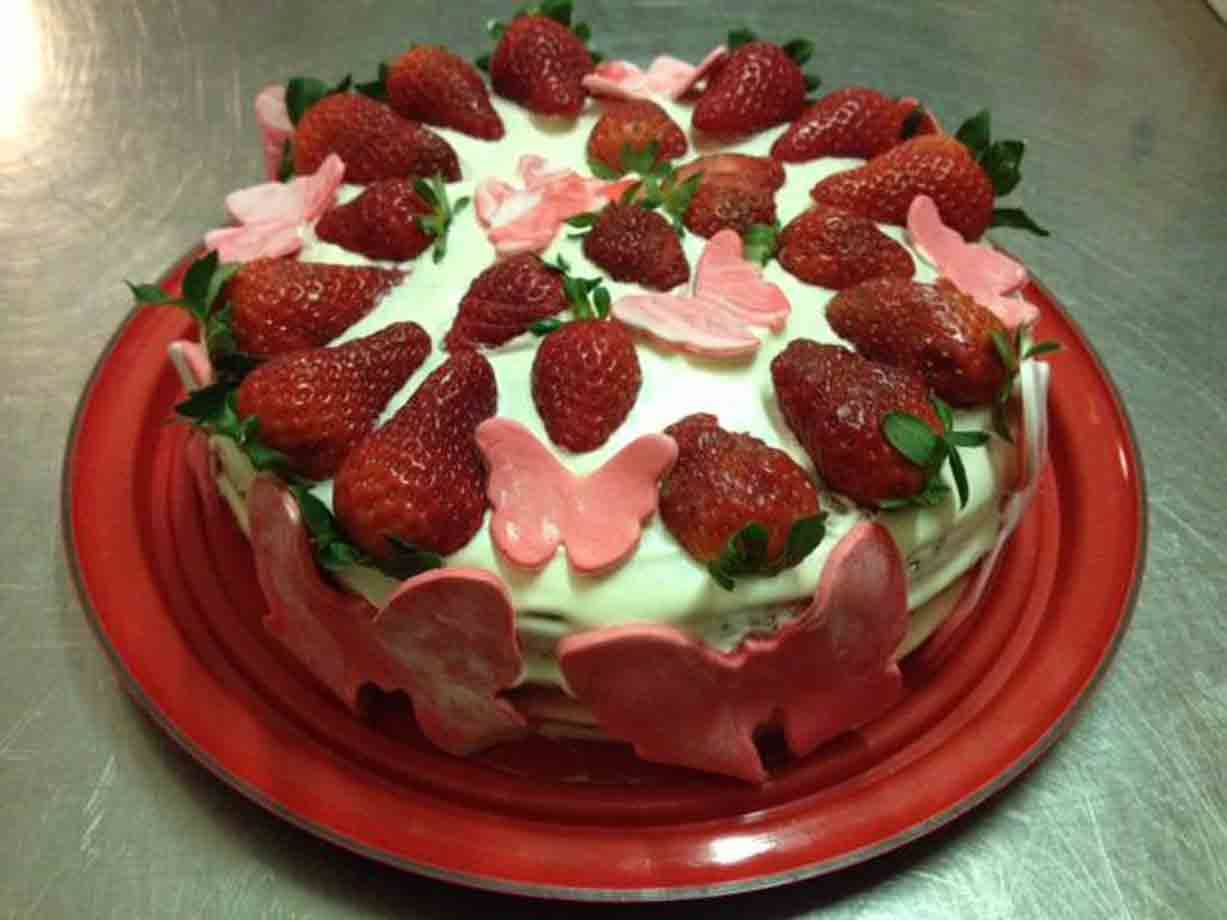 Torta con panna, fragole fresche e farfalle rosa su piatto rosso