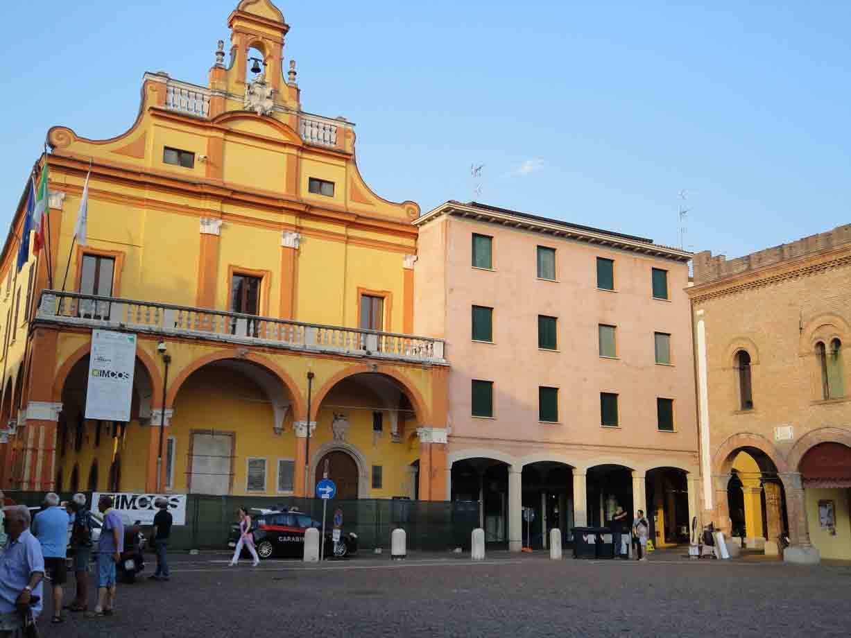 Persone passeggiano in una piazza con un antico palazzo giallo ad archi