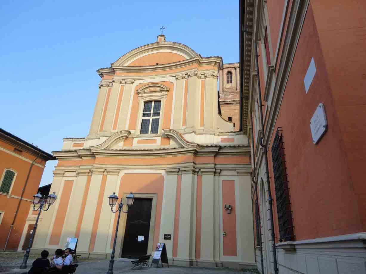 Facciata rosa e ocra di una chiesa barocca, persone sedute sulla piazza