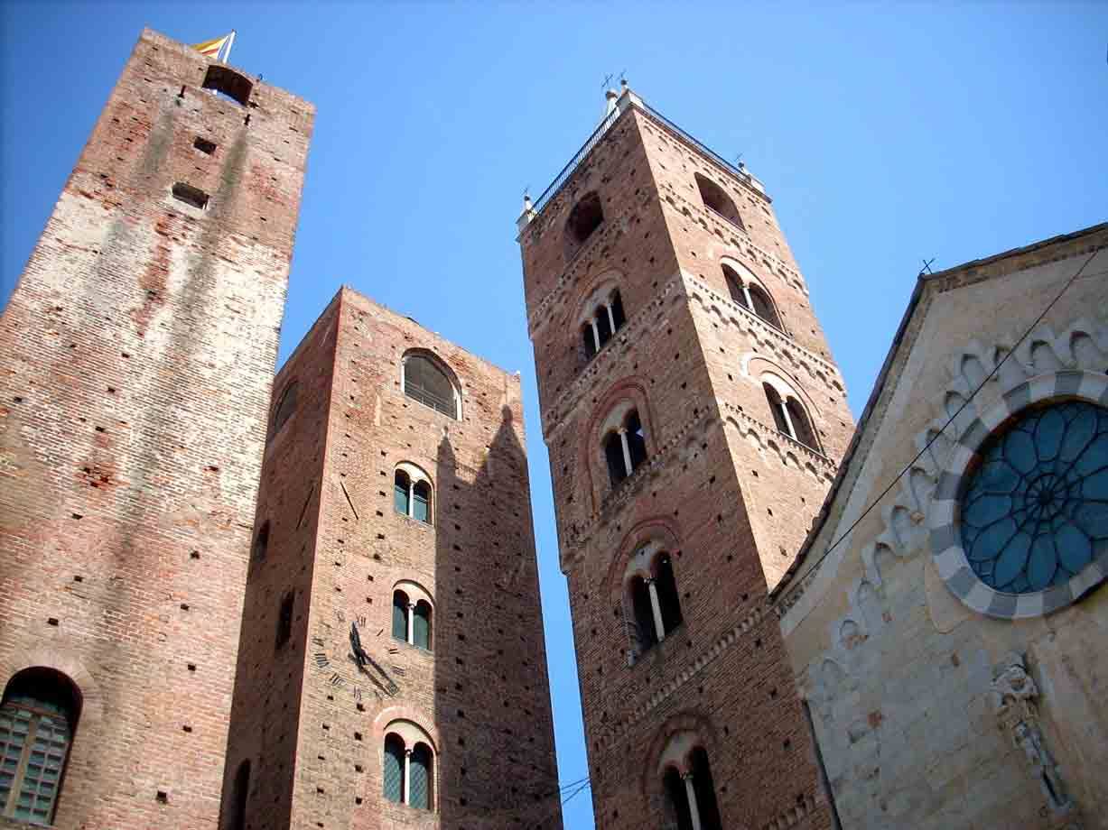 Le torri medievali in mattoni di Albenga e il rosone della cattedrale sotto il cielo azzurro