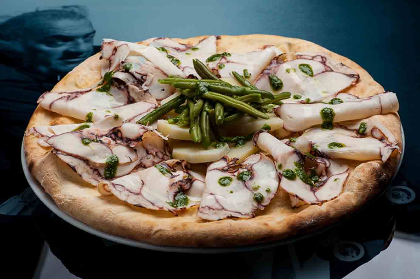 Pizza con triglie, patate e pesto, luce fredda da cucina moderna