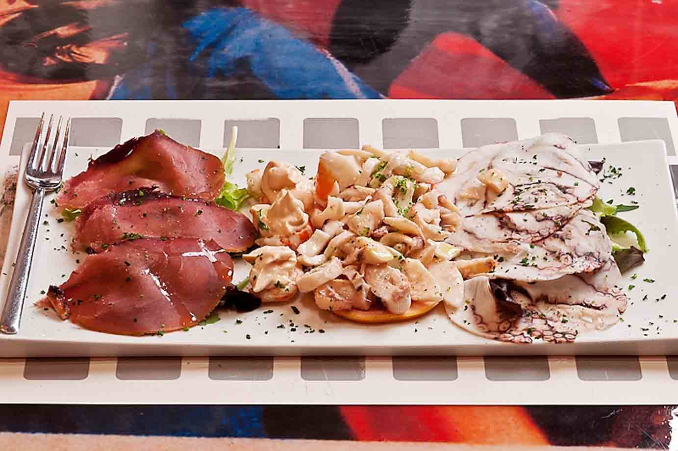 Antipasto misto con bresaola, polpo e insalata di mare su piatto bianco