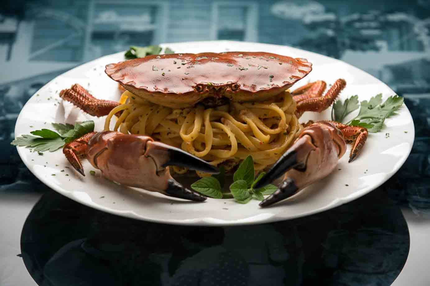 Spaghetti al granchio intero con chele e prezzemolo su piatto bianco