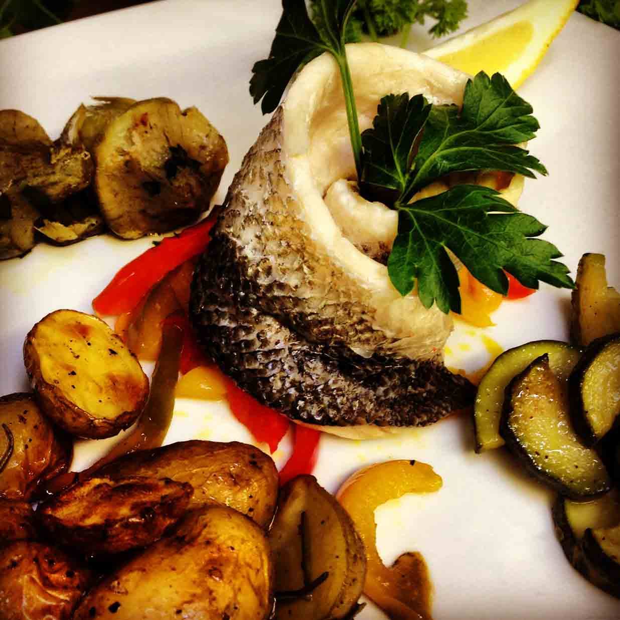 Filetto di pesce con patate arrosto, zucchine e peperoni su piatto bianco