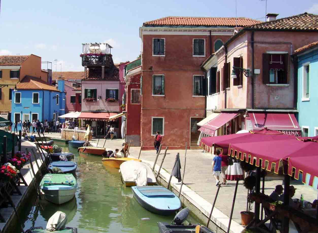 Barche colorate ormeggiate lungo un canale di Burano tra case rosa e azzurre