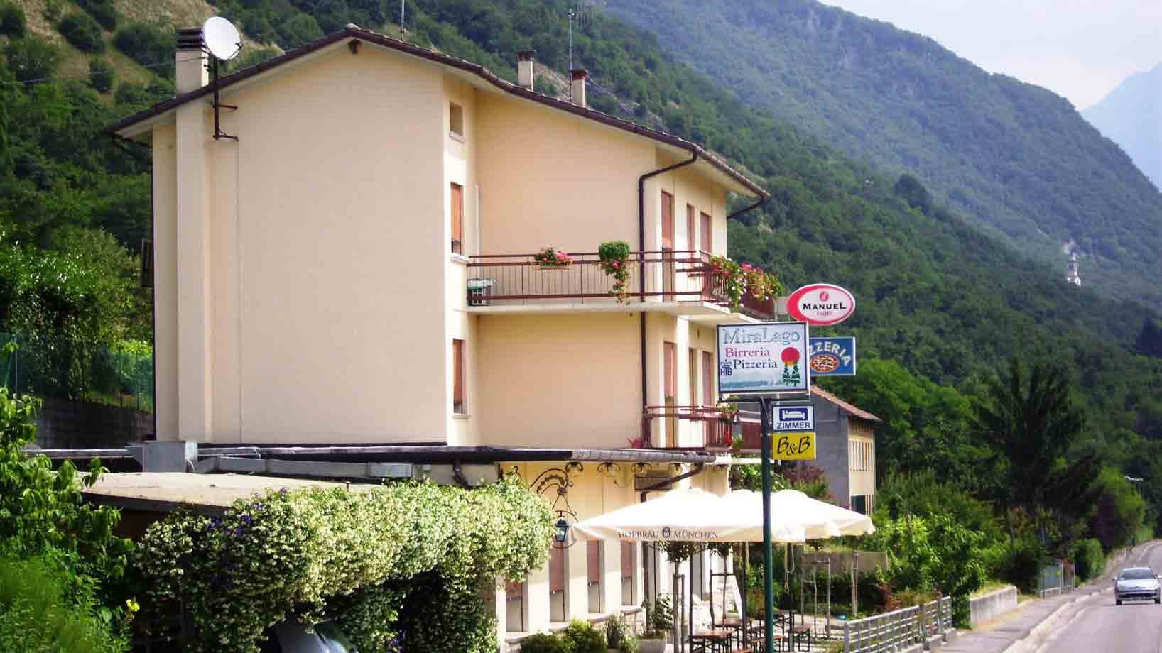 Albergo Miralago con insegna e ombrelloni accanto alla strada, montagna verde dietro