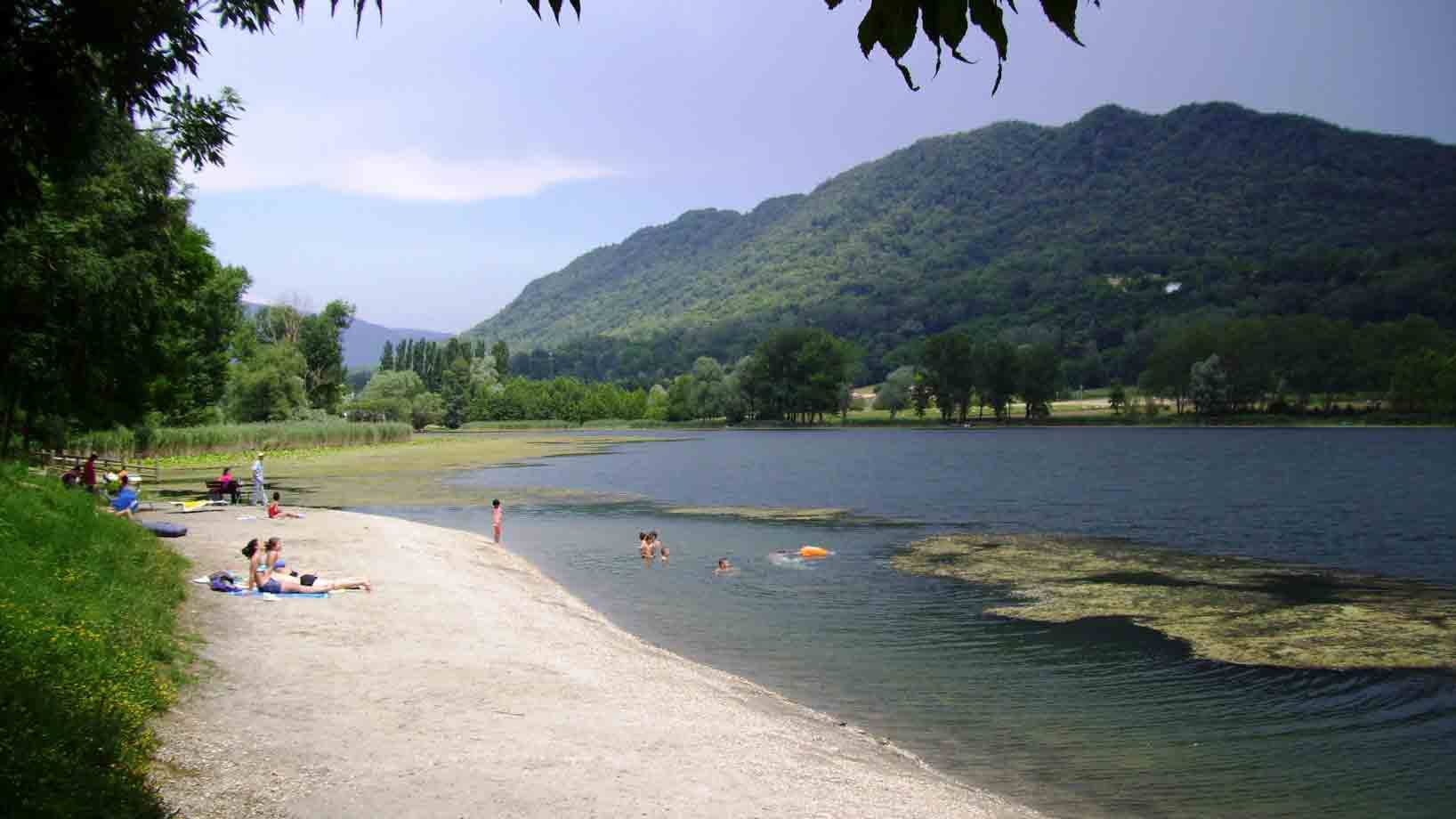 Bagnanti sulla spiaggia sabbiosa del lago, monti boscosi sullo sfondo