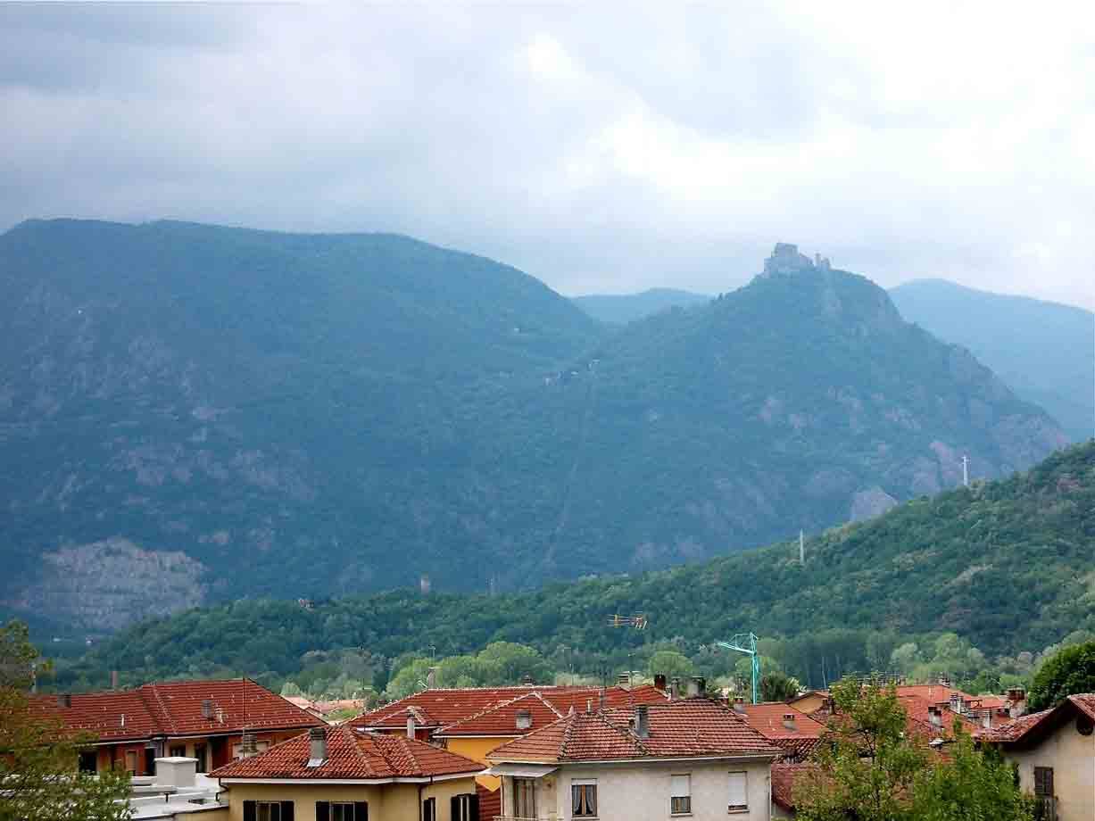 Tetti di tegole rosse davanti a monti verde-blu sotto cielo nuvoloso