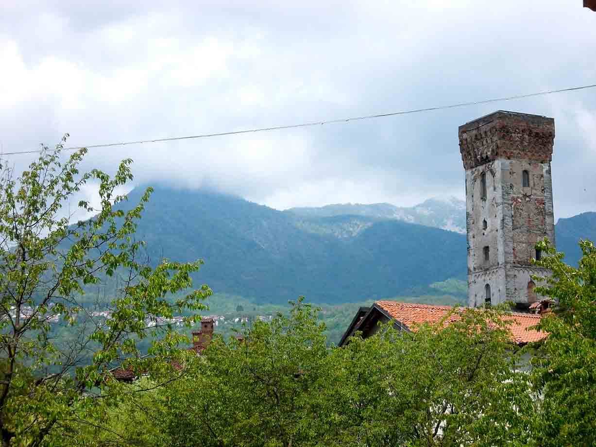 Antica torre in pietra sopra tetti con tegole rosse, montagne avvolte dalle nuvole