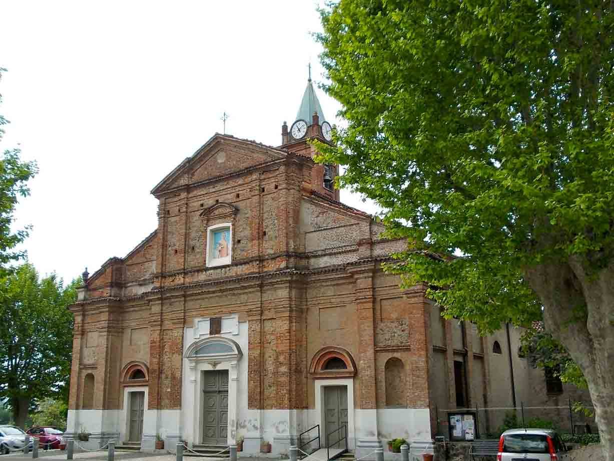 Chiesa in mattoni con campanile e orologio, auto parcheggiate, alberi verdi