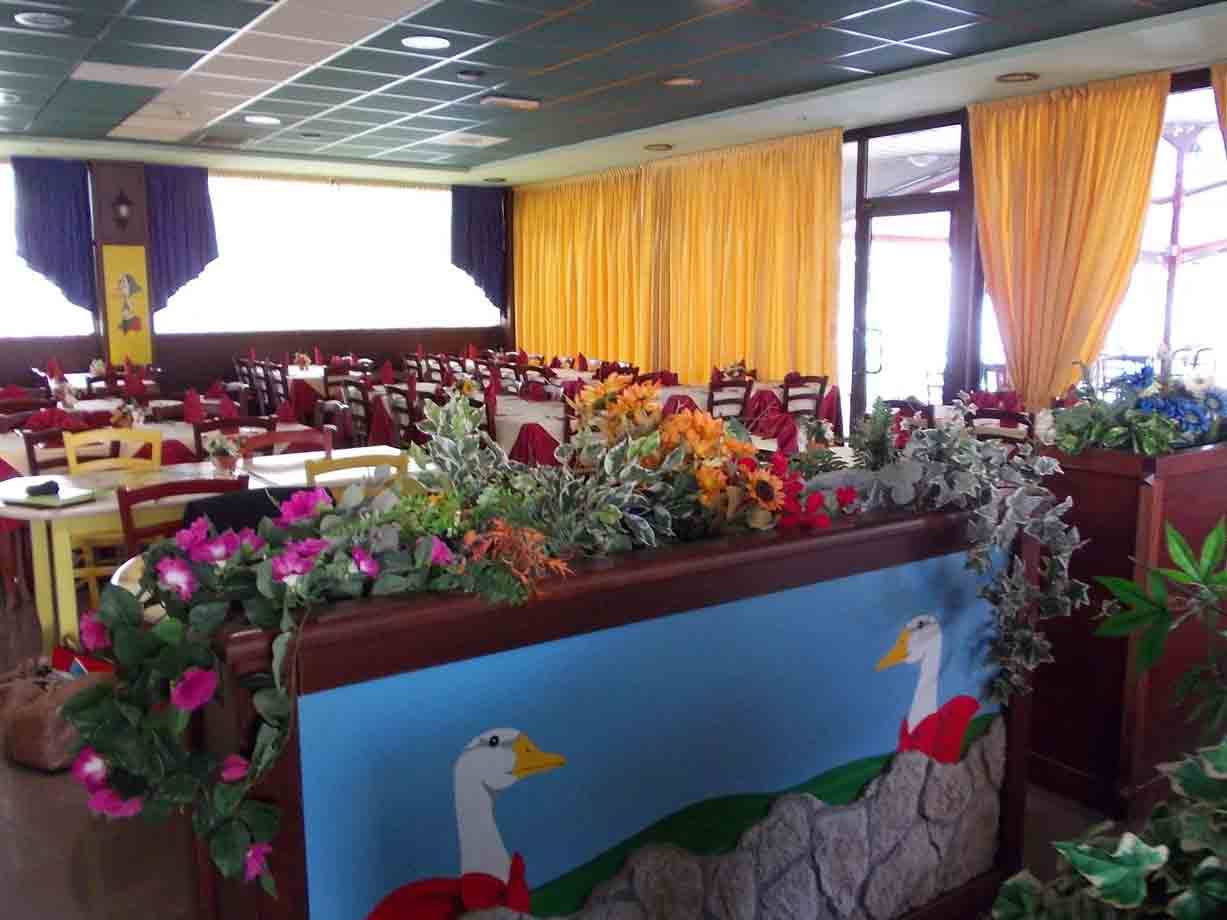 Sala ristorante con tavoli apparecchiati, tende gialle e fiori