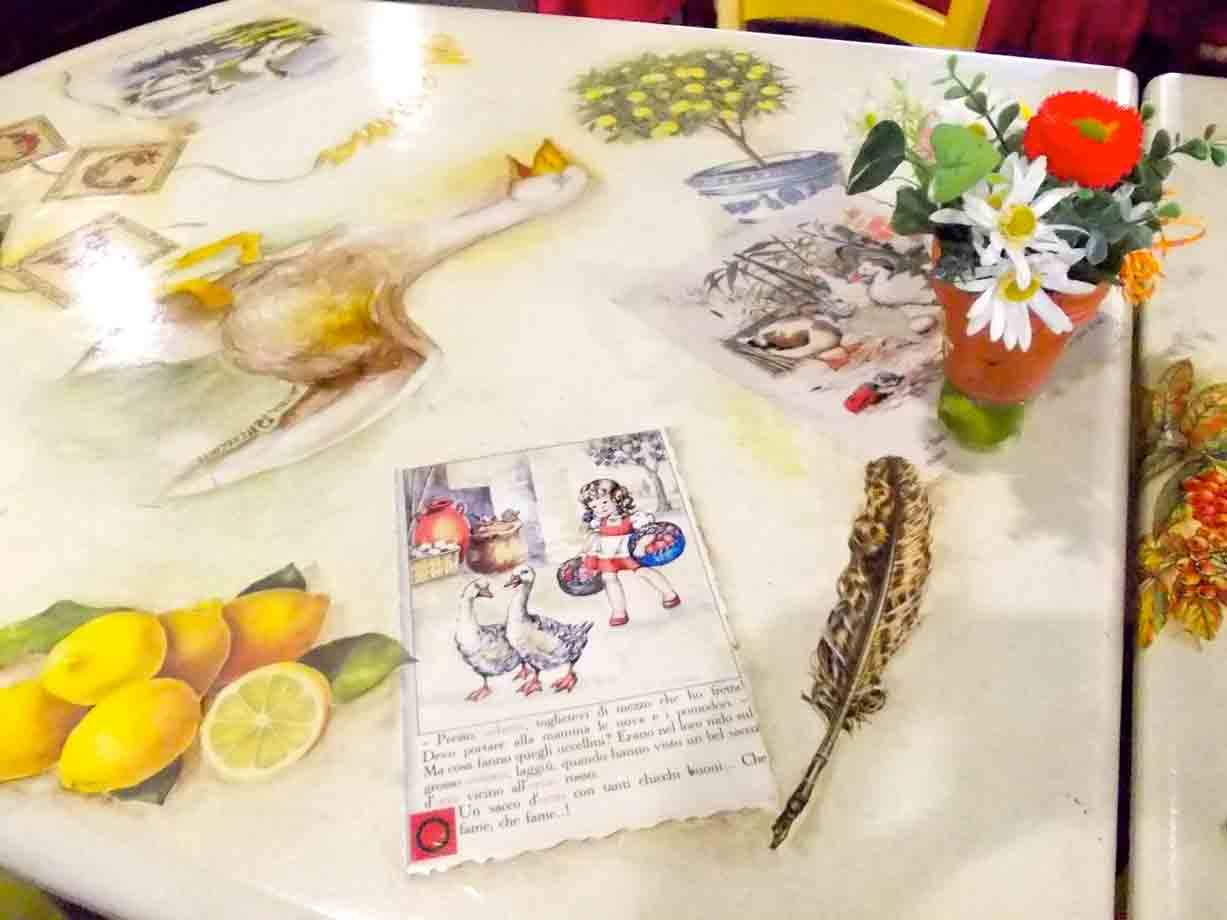 Tavolo decorato con anatra, limoni e piuma, cartolina illustrata e vasetto di fiori