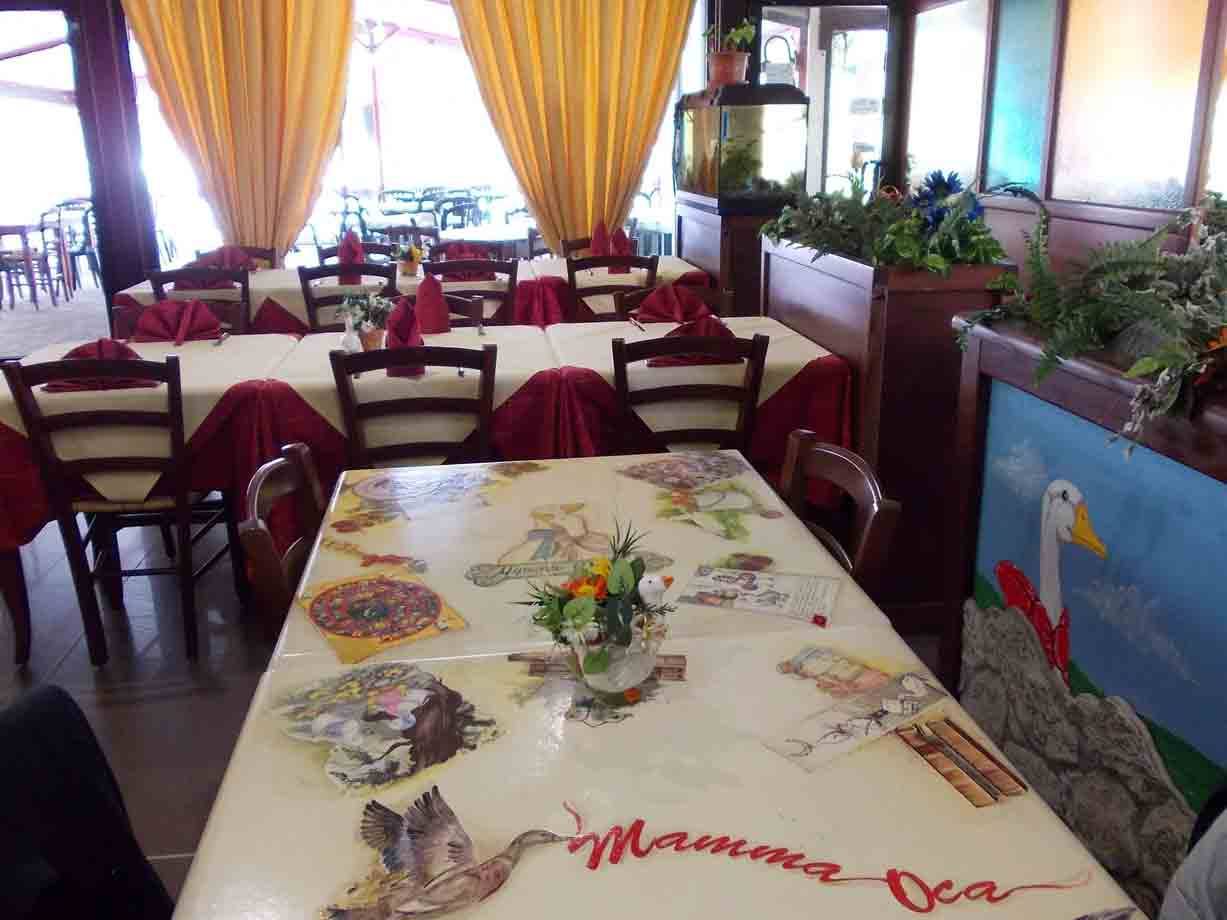 Sala del ristorante Mamma Oca con tovaglie illustrate, tovalli rosse e luce mattutina