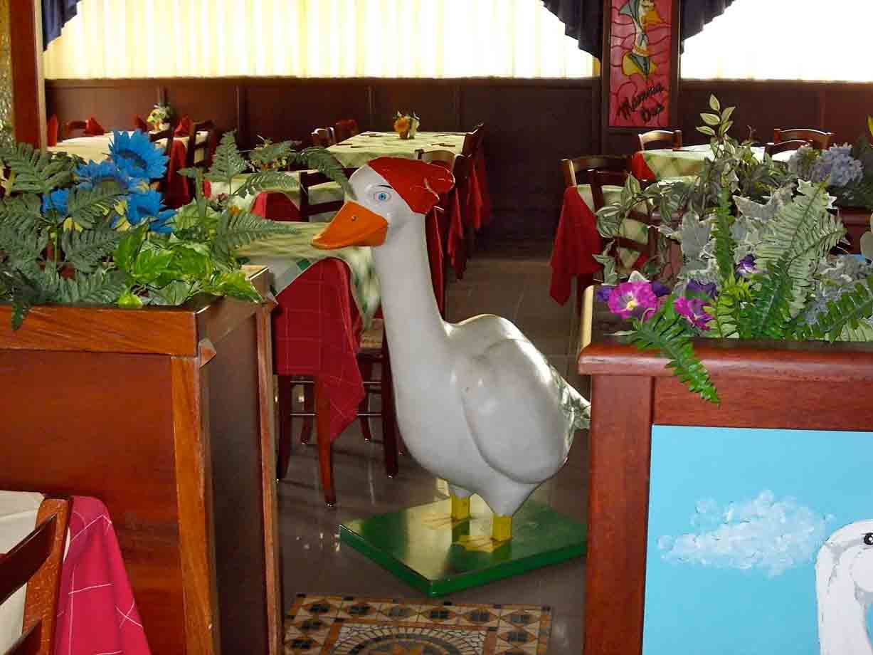 Statua di papera bianca con cappello rosso tra fiori in un ristorante