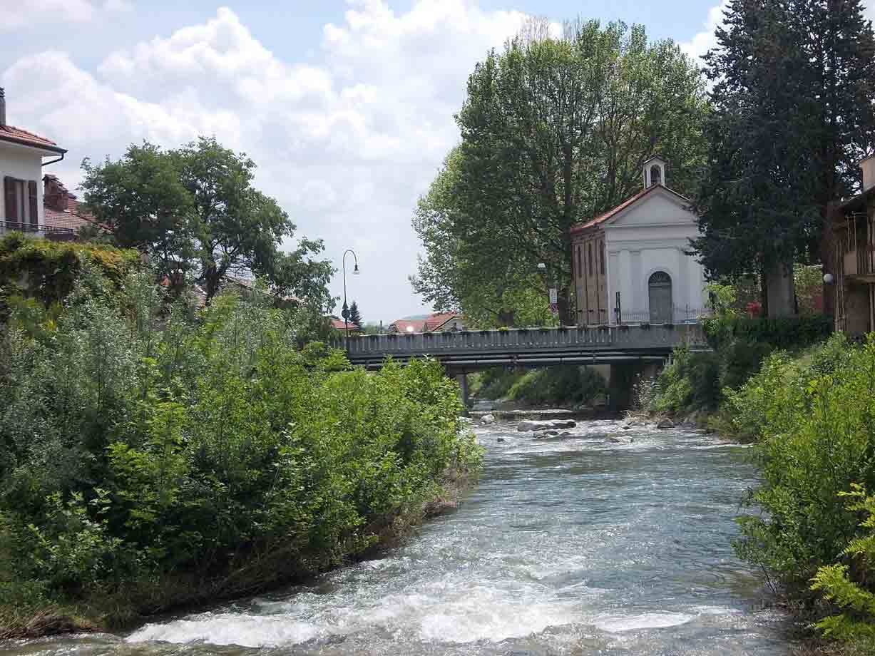 Fiume con acque bianche tra arbusti verdi, ponte e chiesetta bianca con campanile