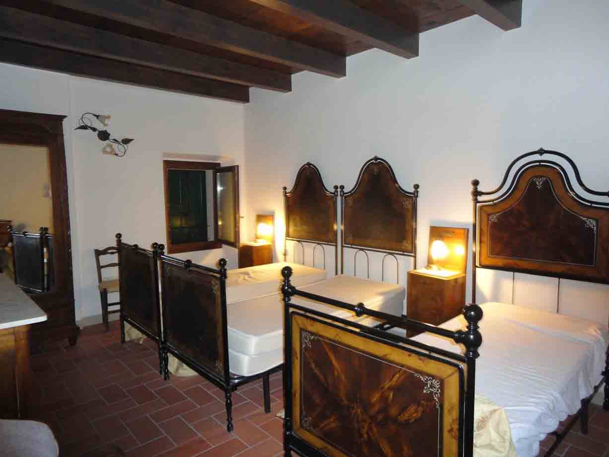 Camere con letti in ferro battuto e legno, luci calde, pavimento in cotto, travi a vista