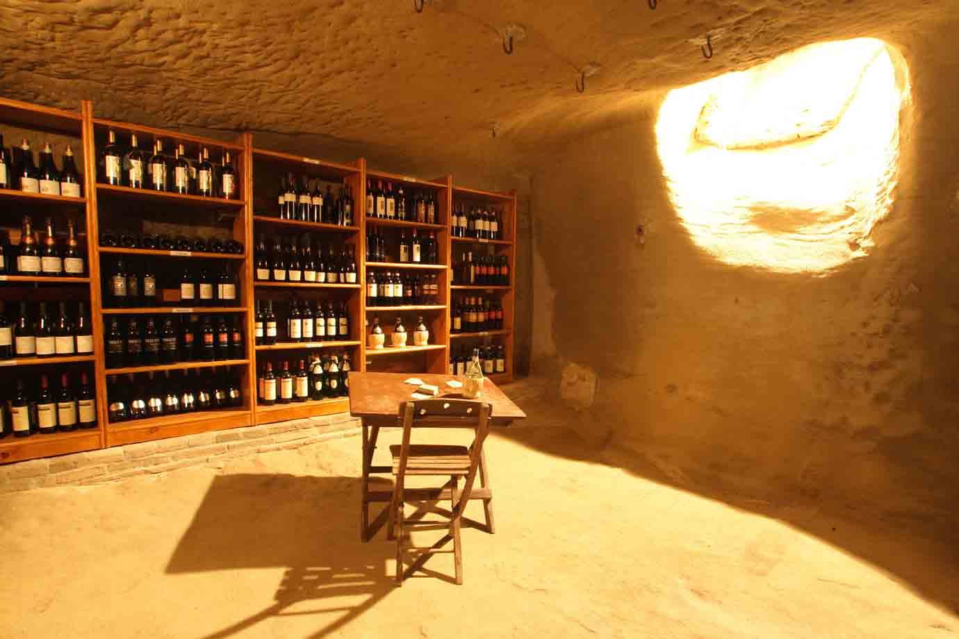 Cantina scavata nella roccia, scaffali di bottiglie, tavolo di legno