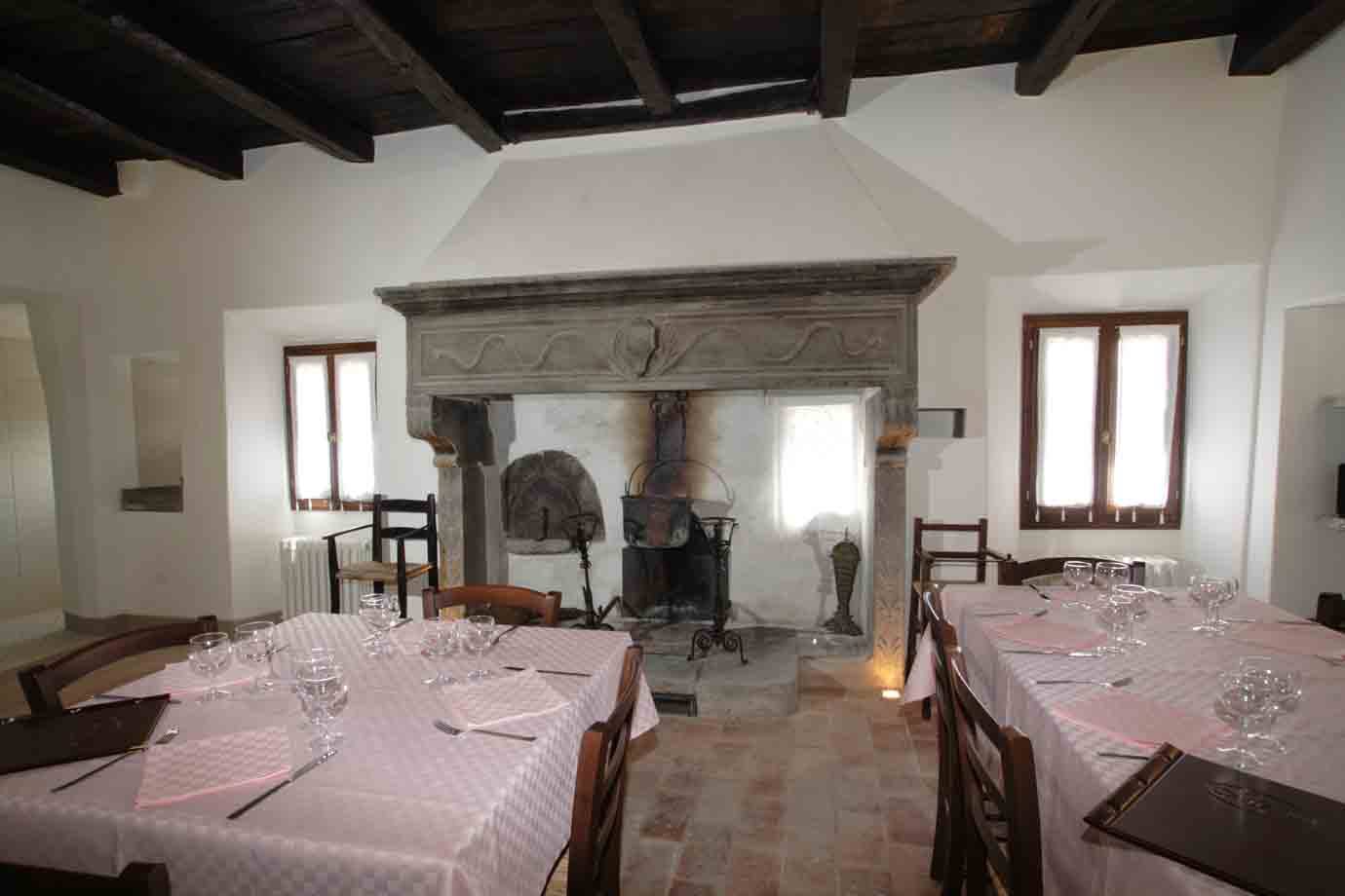 Sala con tavoli apparecchiati e antico camino in pietra tra finestre
