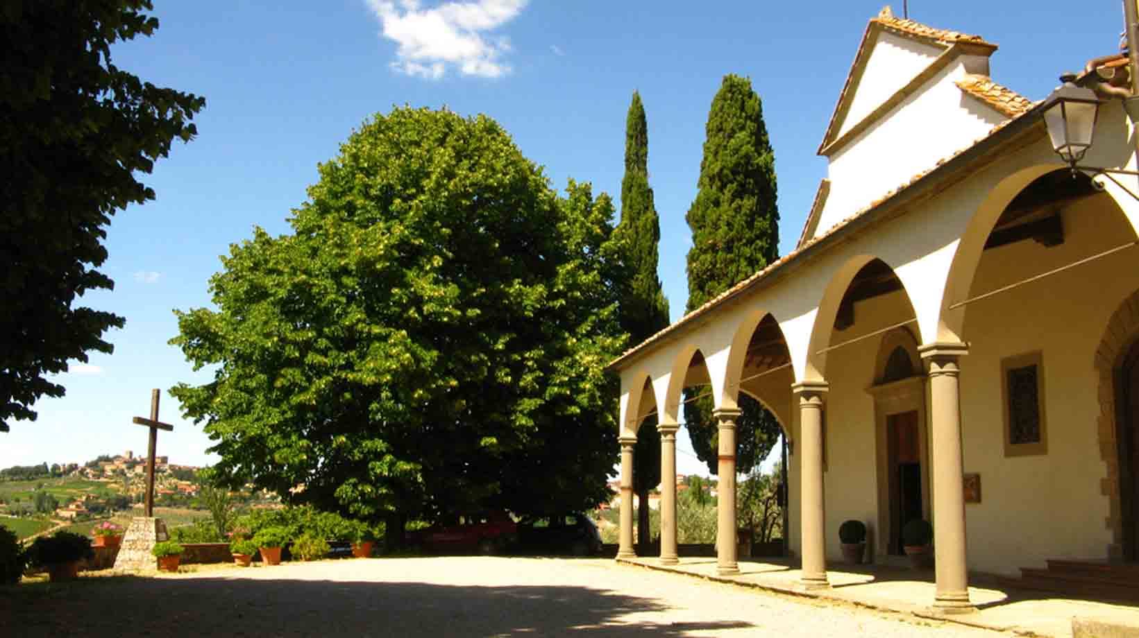 Chiesa bianca con portico di archi e colonne, cipressi e croce di legno