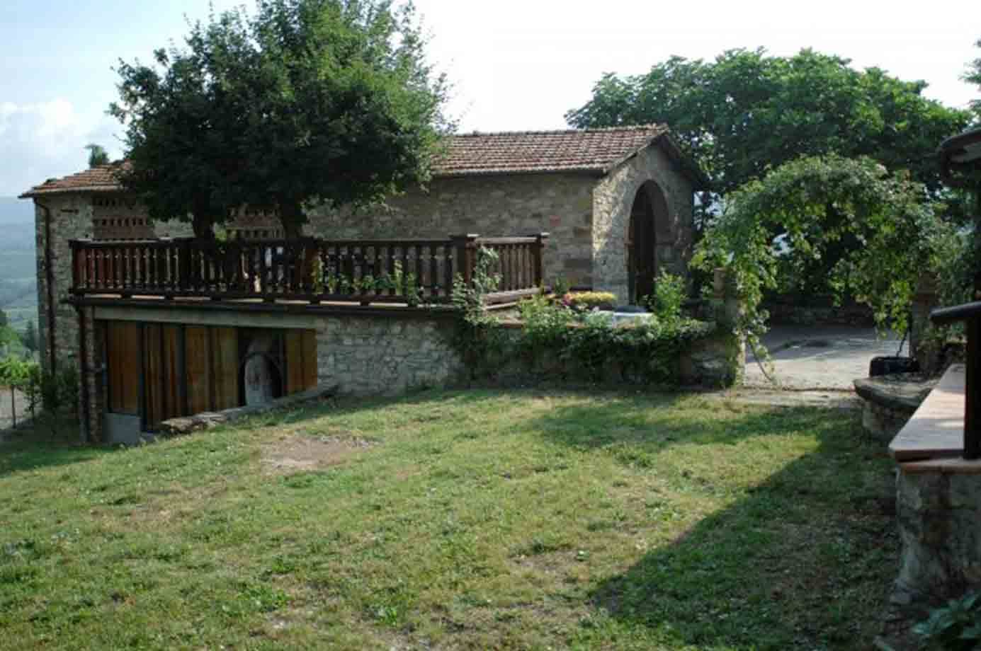 Casa rurale in pietra con terrazza in legno e prato verde davanti