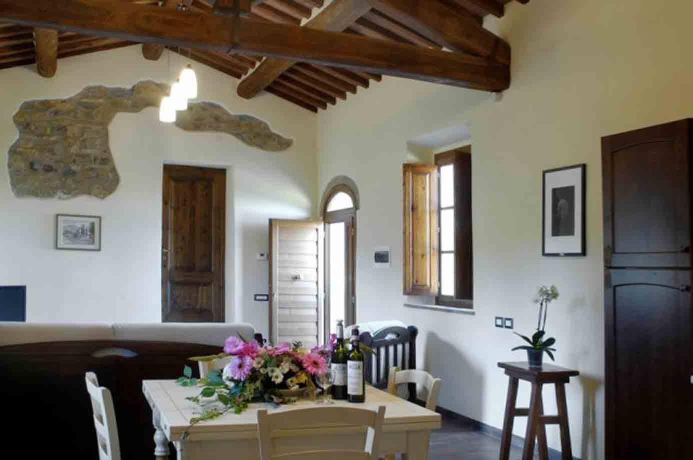 Sala rustica con travi in legno, pietra a vista, tavolo con fiori e vino