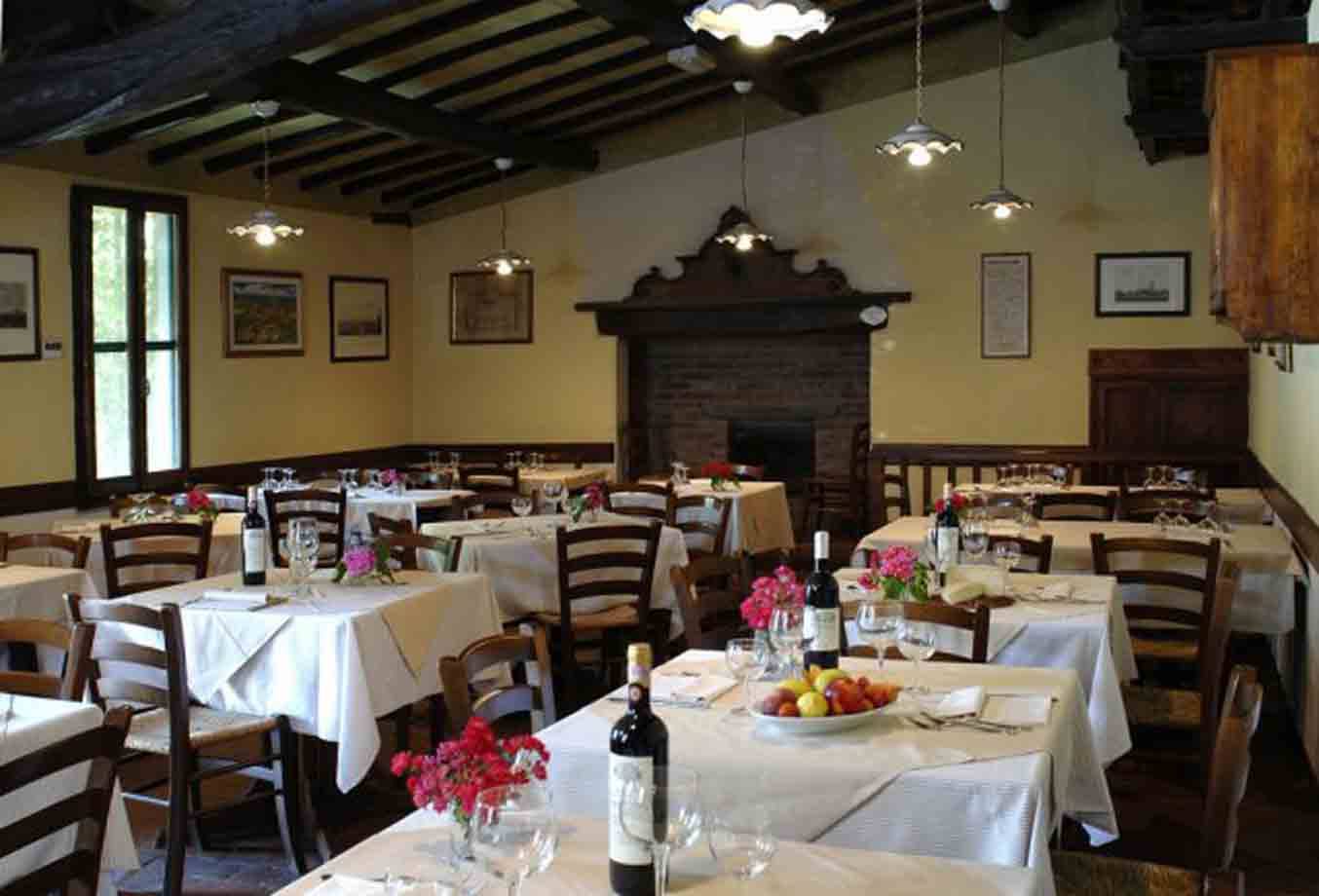 Sala di trattoria con tavoli apparecchiati, vino, fiori e caminetto in mattoni