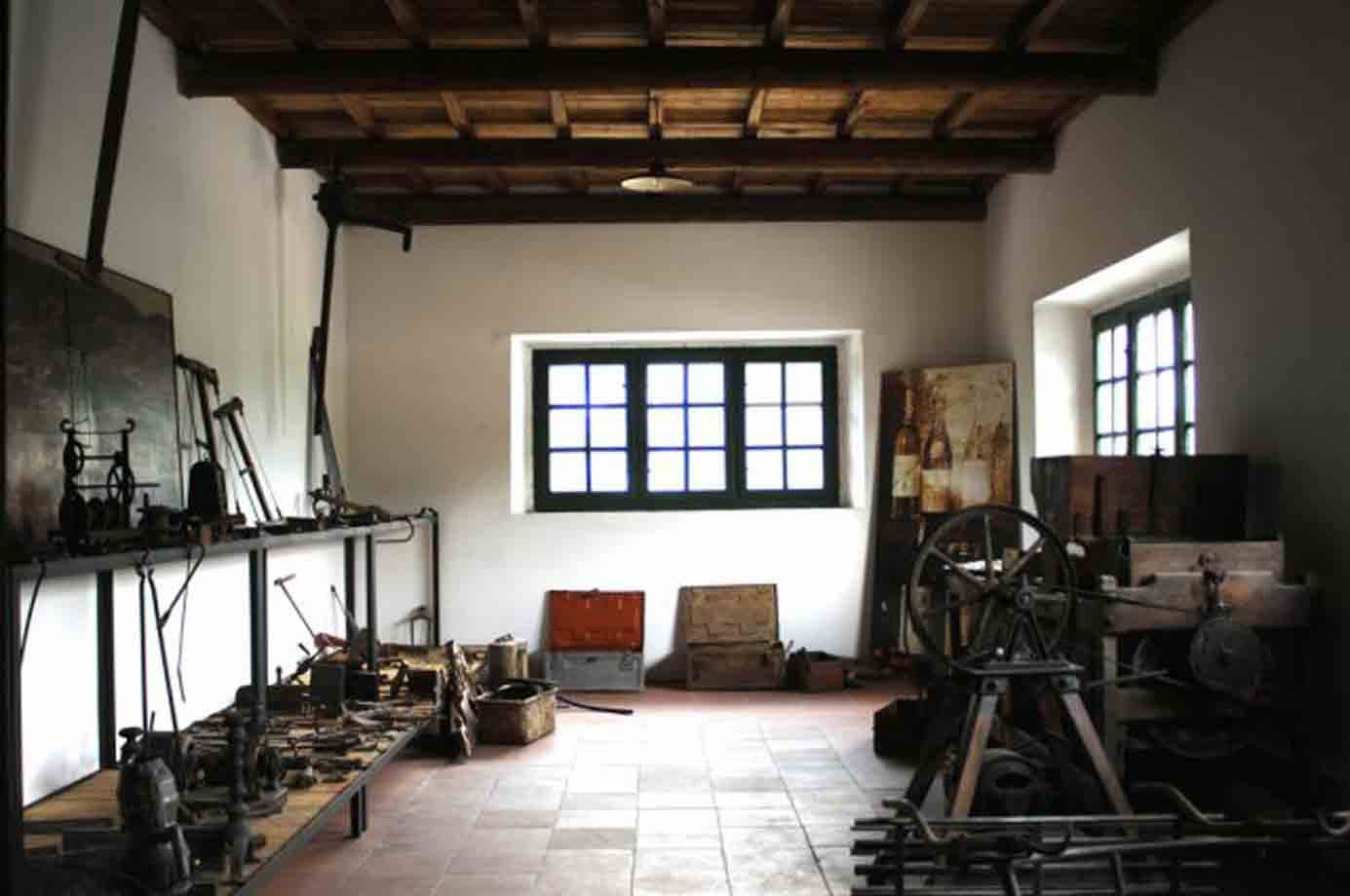 Antica bottega con attrezzi in ferro, muri bianchi, soffitto a travi e finestre