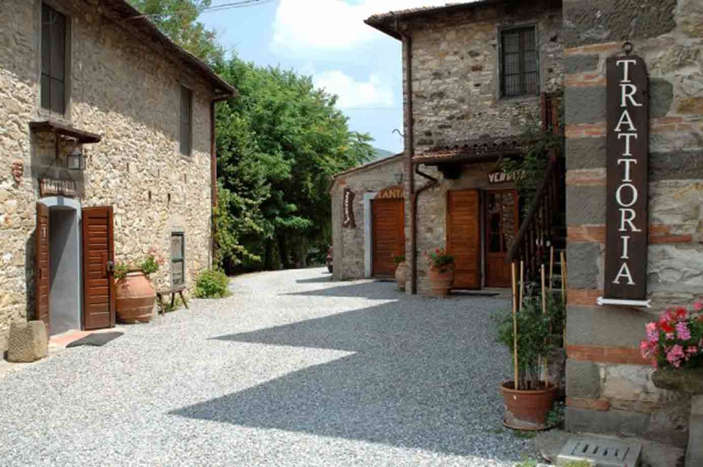 Borgo di pietra con stradina ghiaiosa e insegna della trattoria