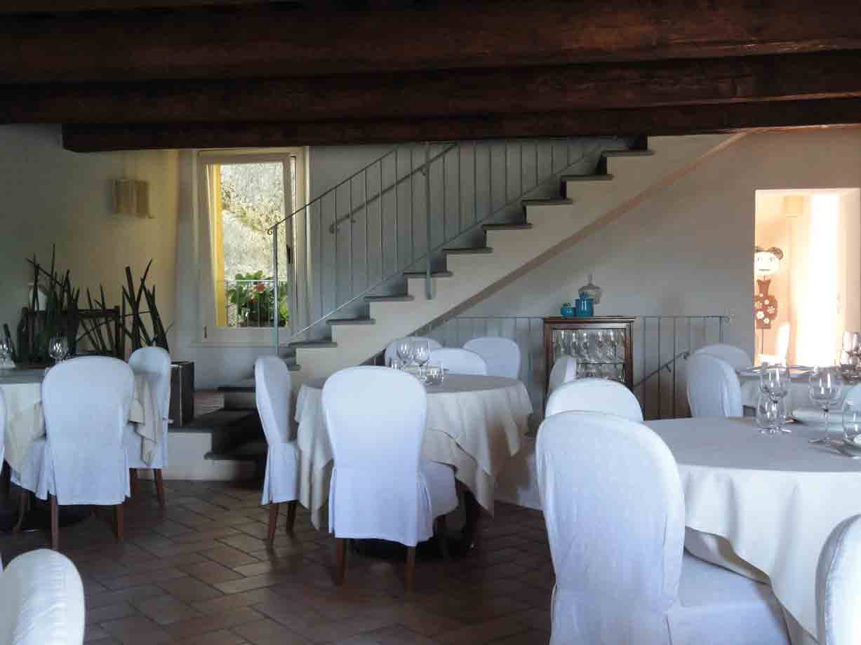 Sala ristorante con tavoli apparecchiati, sedici coperte di bianco e scala interna