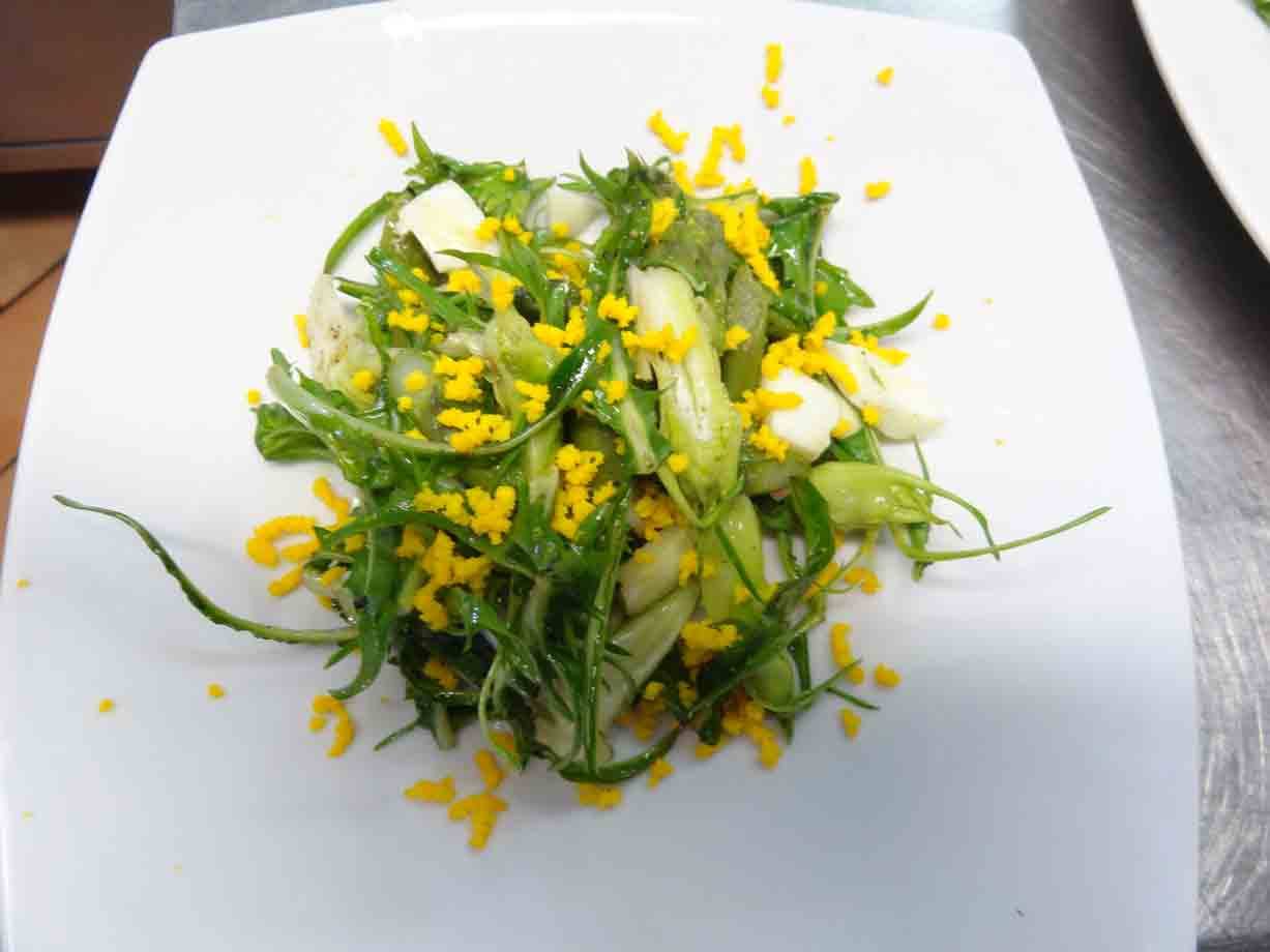 Insalata verde con uovo sbriciellato su piatto bianco quadrato