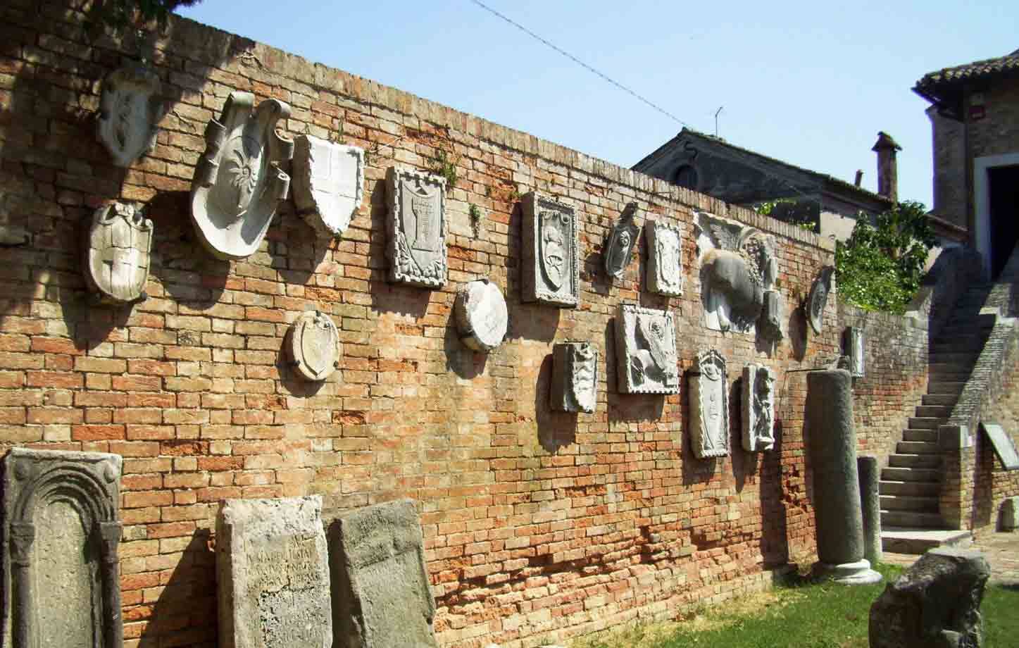 Stemmi e lapidi in pietra incastonati su muro di mattoni, scalinata a destra