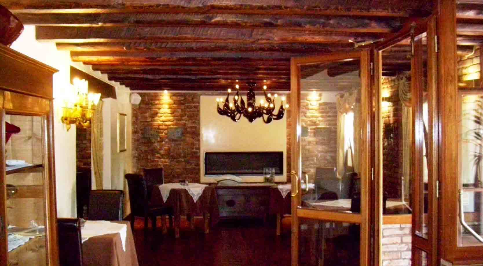 Sala di ristorante con travi in legno, lampadario nero, tavole apparecchiate e muri in mattoni