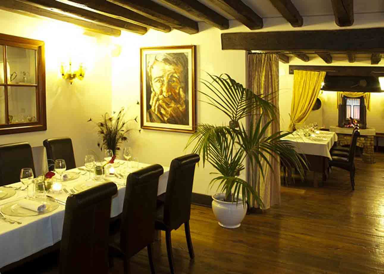 Sala di ristorante con travi in legno, tavole apparecchiate, palma in vaso e quadro