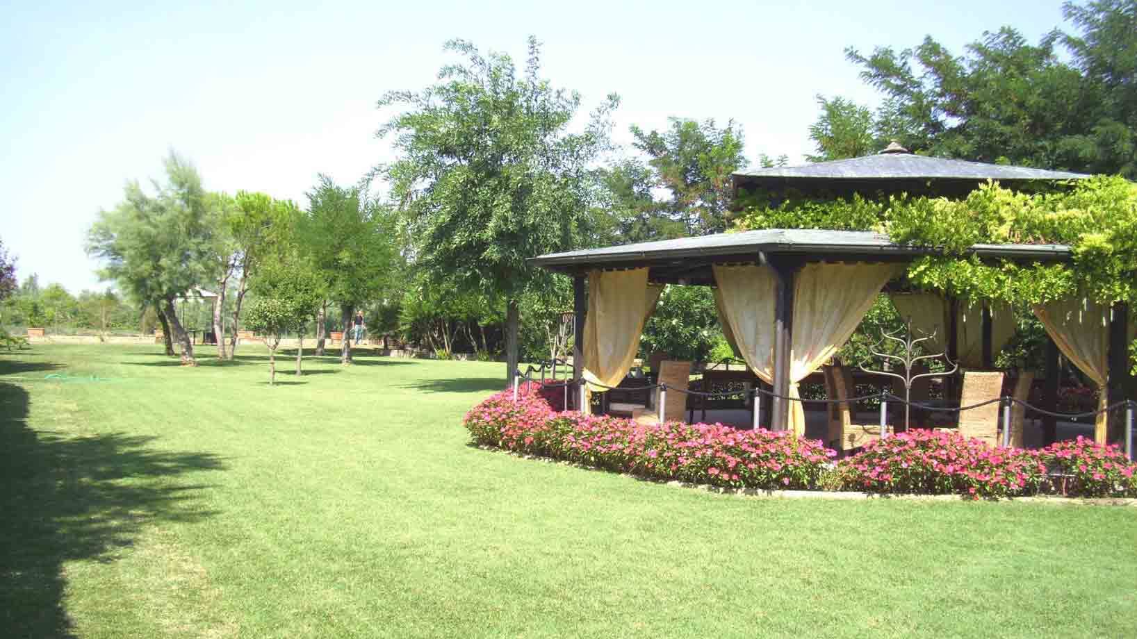 Gazebo con tende e fiori rosa in un giardino verde assolato