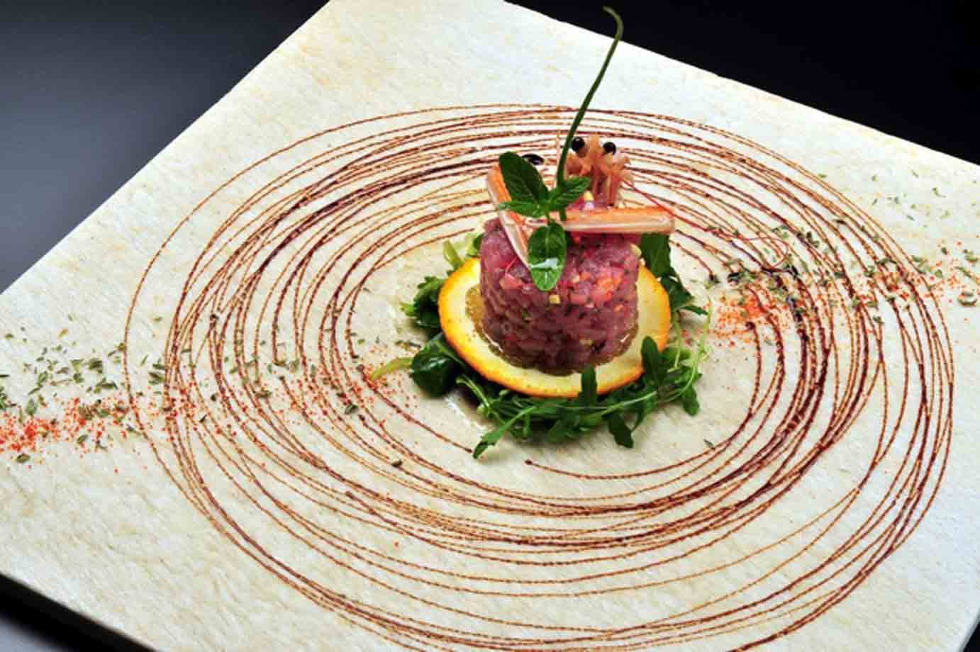 Tartare di tonno su piatto di pietra, decorata con spirali di salsa e menta