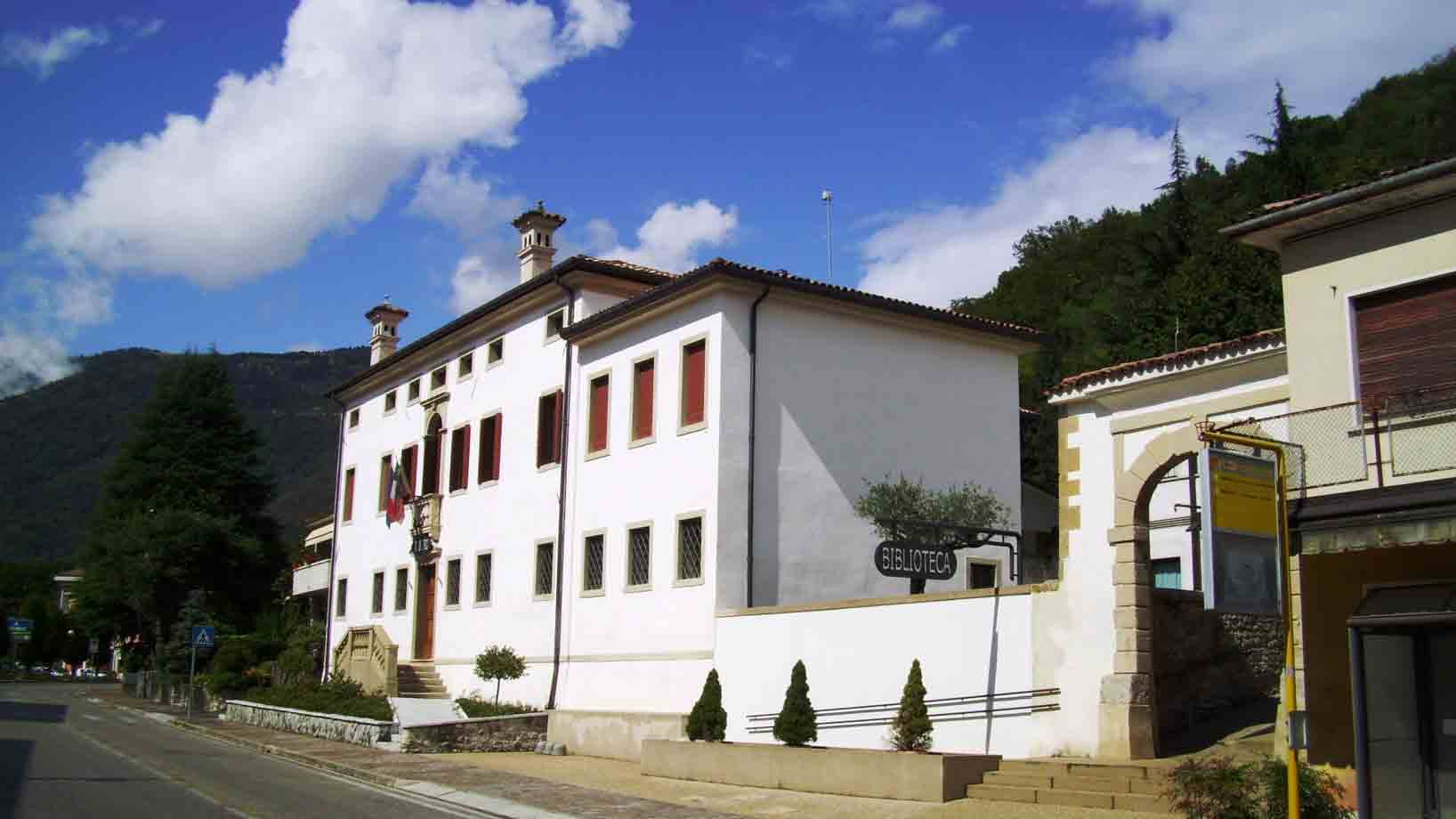 Palazzo bianco con insegna del seminario, monti boscosi e cielo nuvoloso