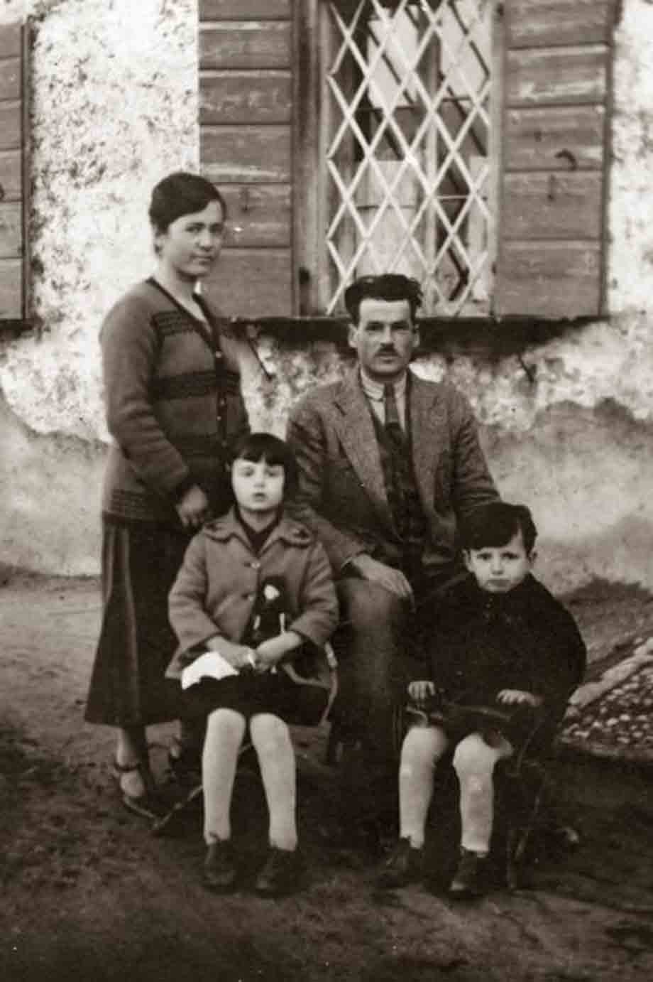 Famiglia di quattro posa davanti a casa rurale con finestre in legno, foto d'epoca