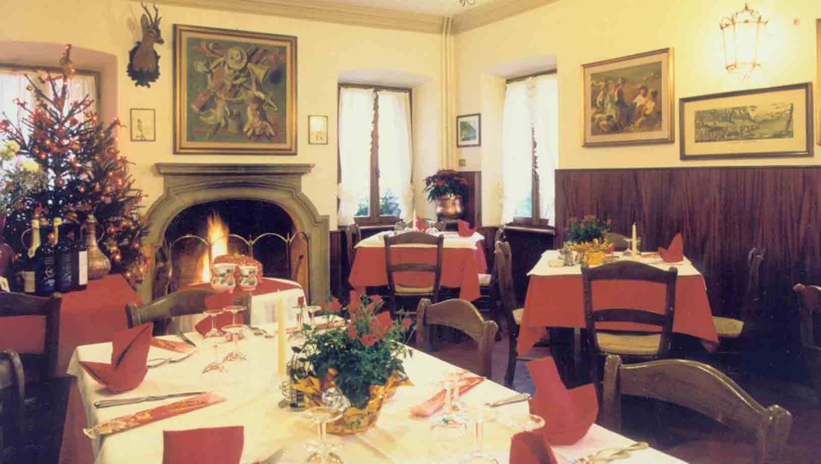 Sala di ristorante con tavoli apparecchiati, caminetto acceso e albero di Natale