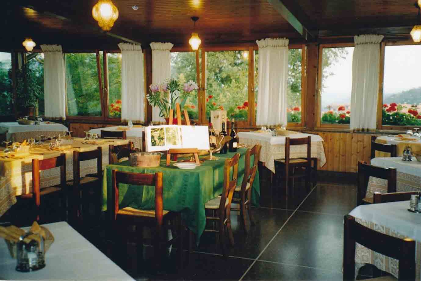 Sala di ristorante con tavoli apparecchiati, tovaglie verdi e finestre sui fiori