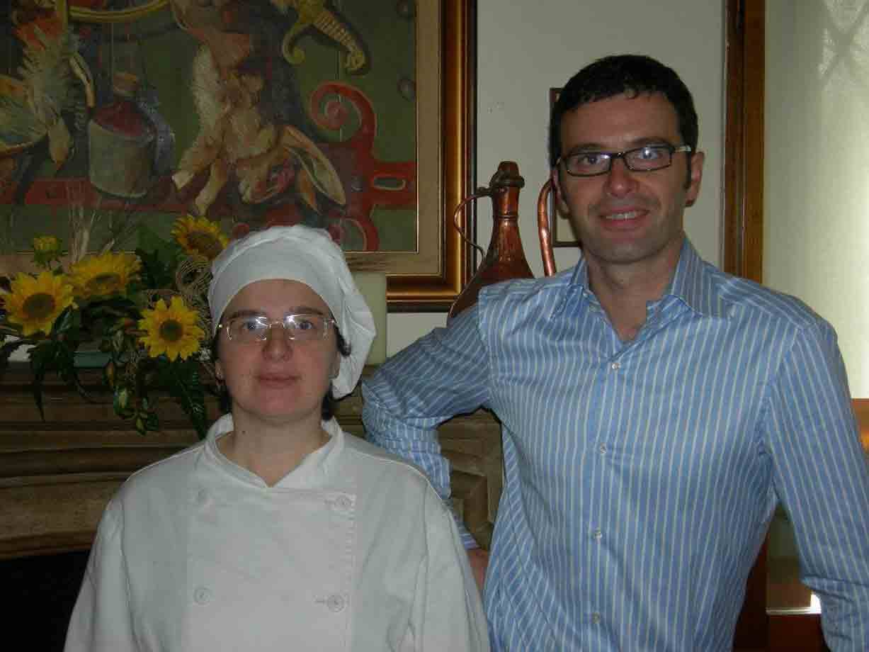 Cuoca in uniforme bianca accanto a un uomo in camicia a righe, caminetto con girasoli