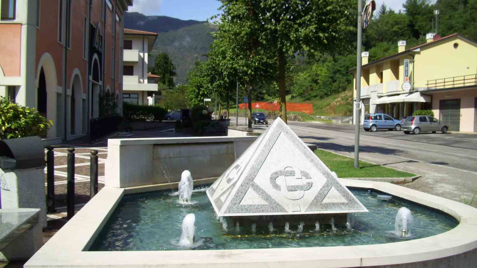 fontana circolare con piramide di marmo, getti d'acqua, piazza con auto