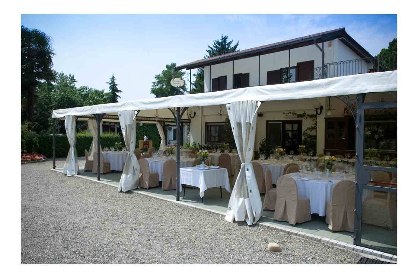Tenda bianca con tavoli apparecchiati e seggiole coperte davanti a una villa