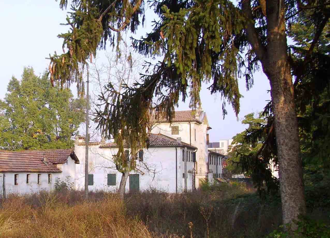 Cascina bianca con tetto in coppi tra abeti e erba secca